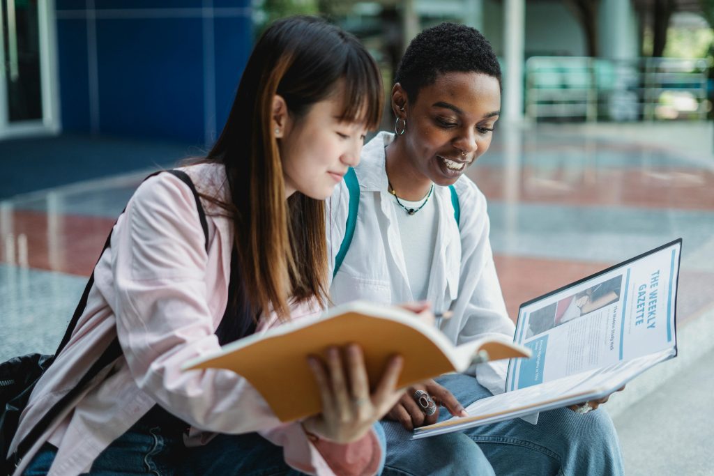 Two women happily studying and sharing knowledge outdoors in a bright, urban environment.